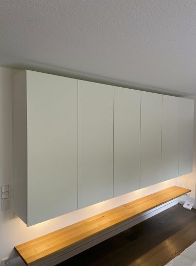 Hängeschrank XXL Ein Hängeschrank über eine komplette Wandbreite. Unter dem Hängeschrank befinden sich Spotlichter, welche eine Eichenablage anstrahlen.
