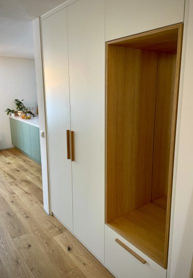 Garderobenschrank Moderner Garderobenschrank gefertigt aus weißen Platten in Kombination mit furnierter Eiche. Ein offener Bereich dient als Sitzgelegenheit.